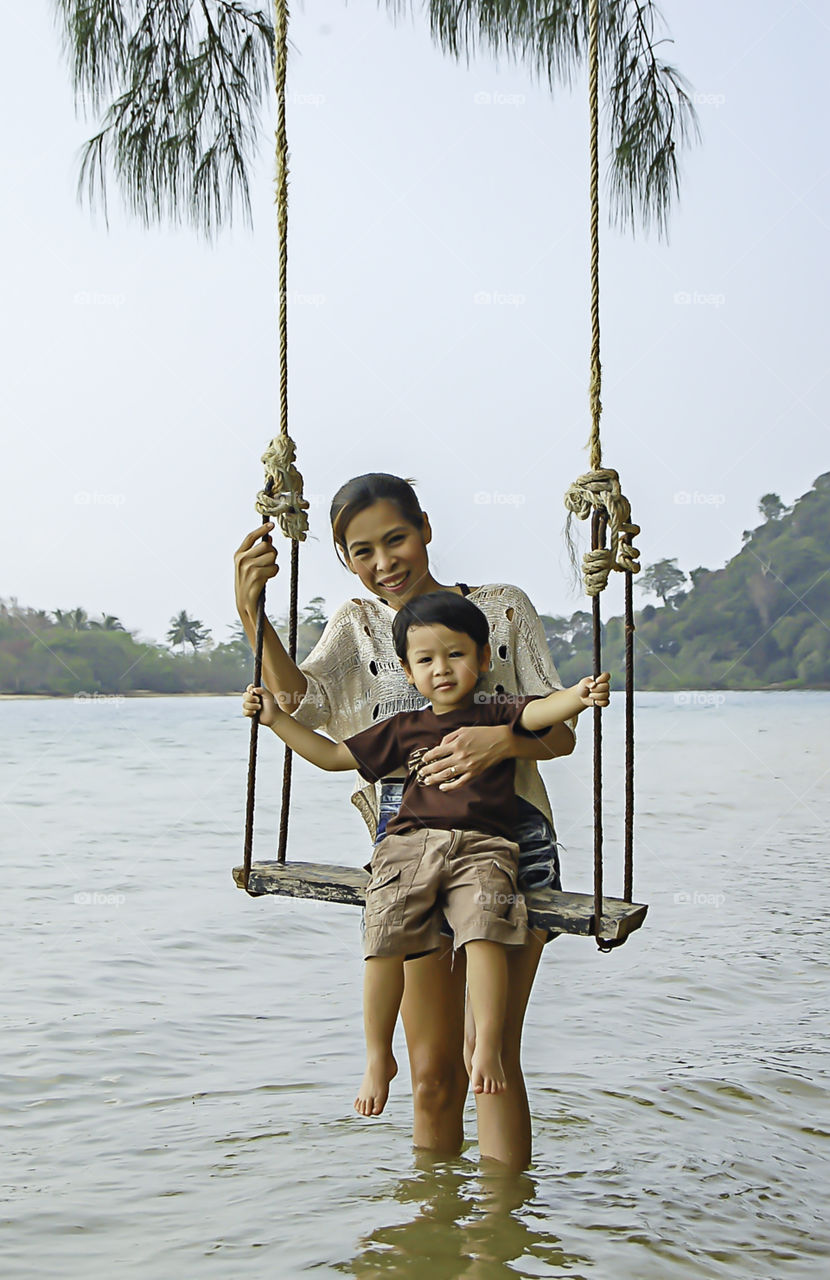 Portrait of mother and son playing swing chair in the sea.