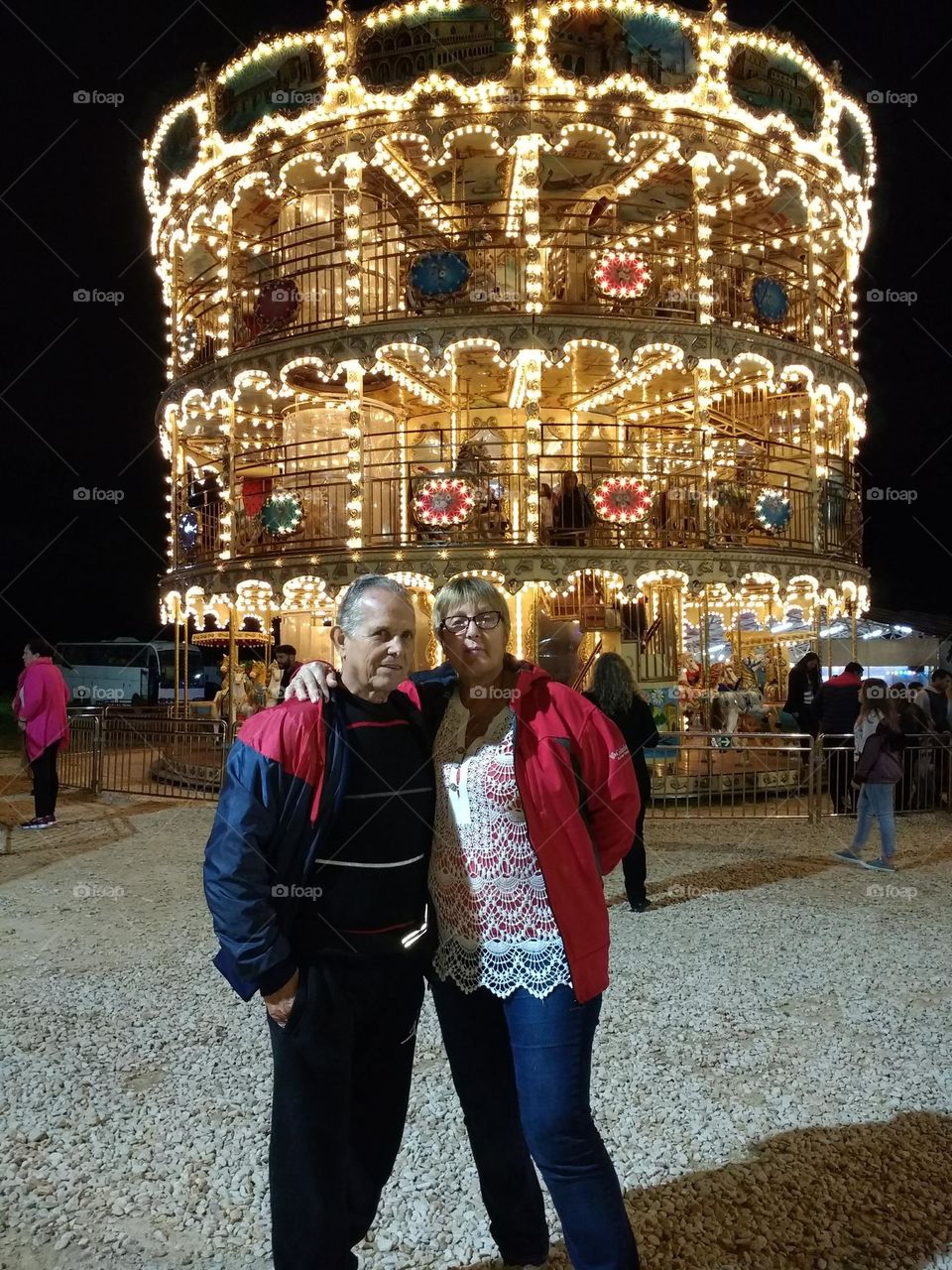 un hombre mayor y una señora mayor con el fondo de un carrusel con la luces encendidas de noche