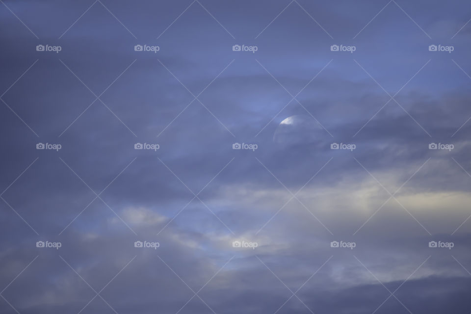 Full Moon on the morning sky behind the clouds.