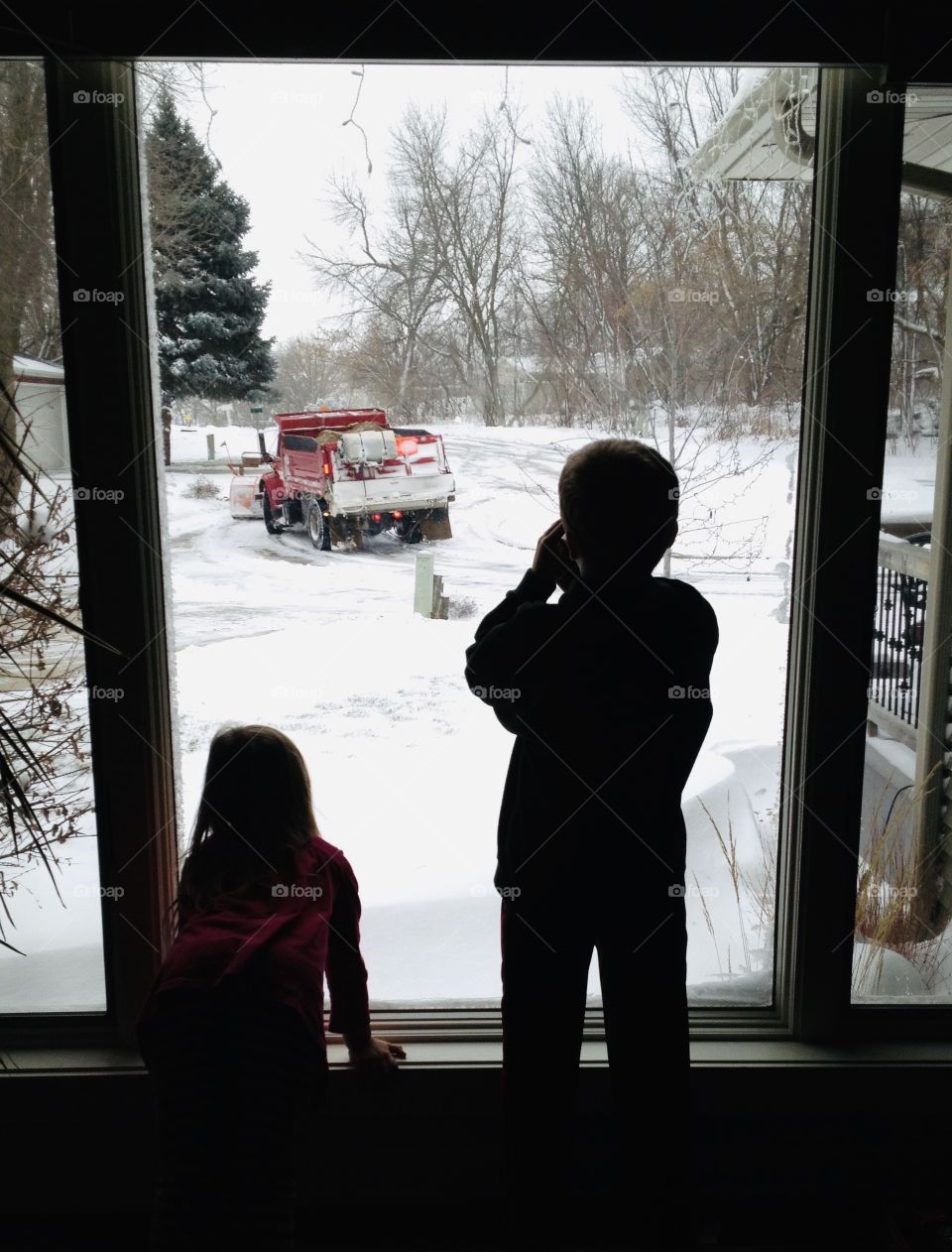 Two children watching snowplow out in the cul de sac plowing all of the snow into a pile! 