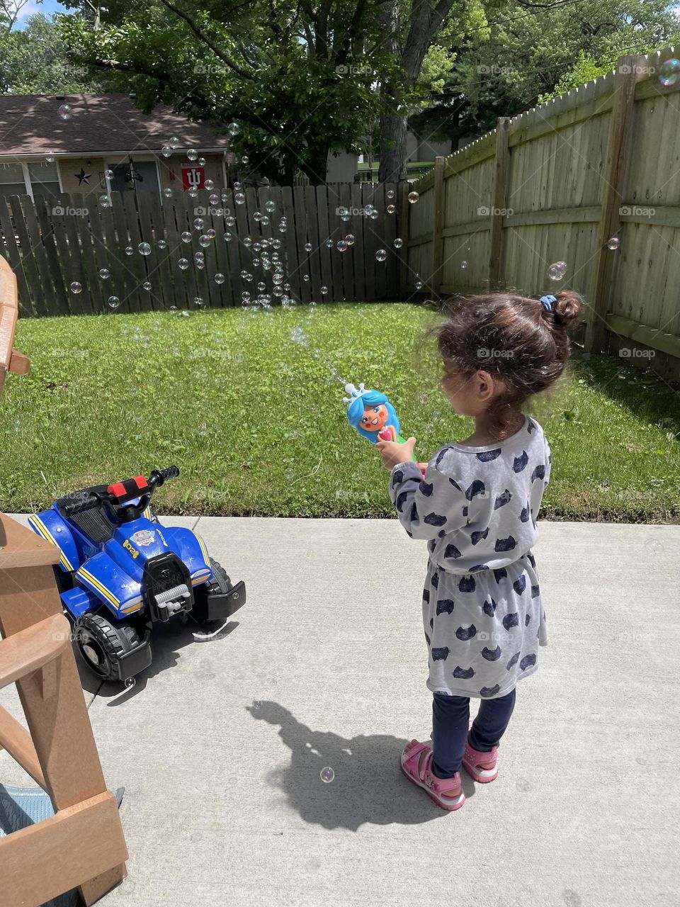 Toddler girl plays with bubbles in the back yard, little girl having fun with bubble maker, summertime fun with toddlers 