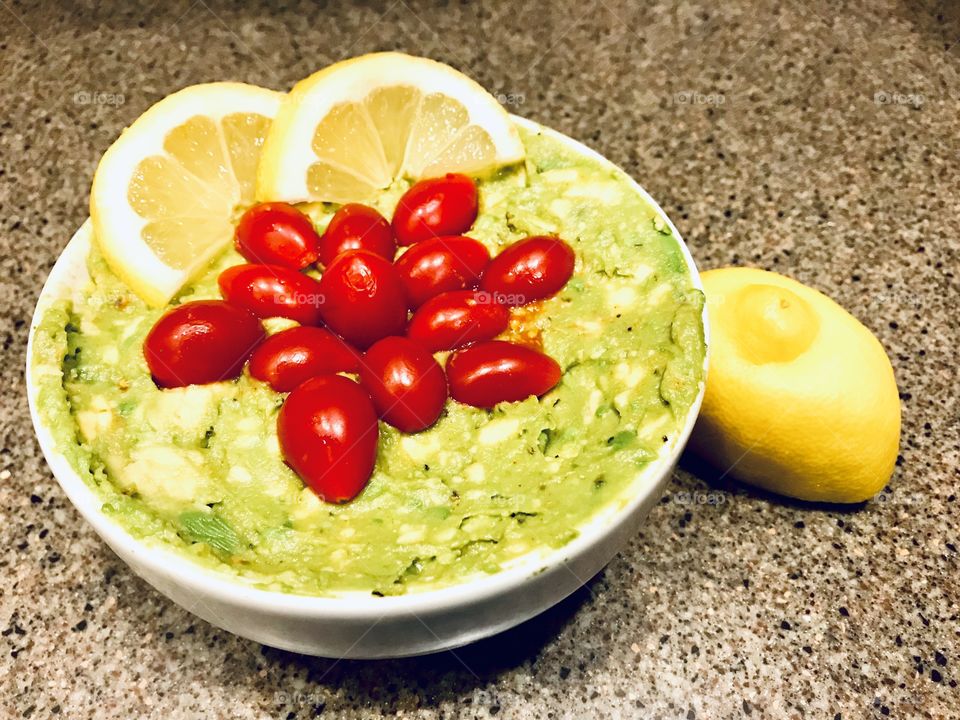 Delicious guacamole with beautiful red grape tomatoes and lemon slices on top made by a child!! 