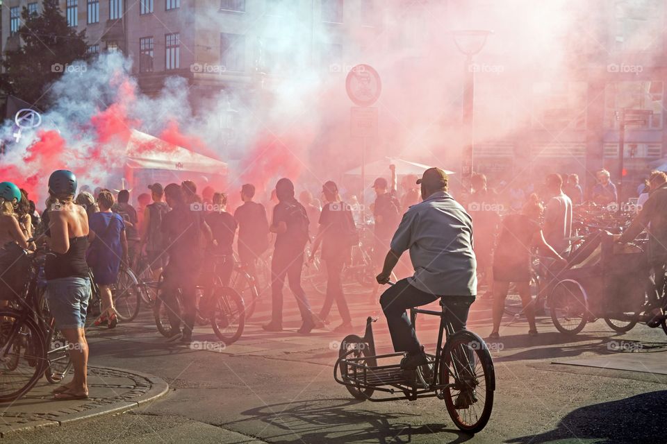 Man on a three wheeled black bike at a demonstration with red and white smoke