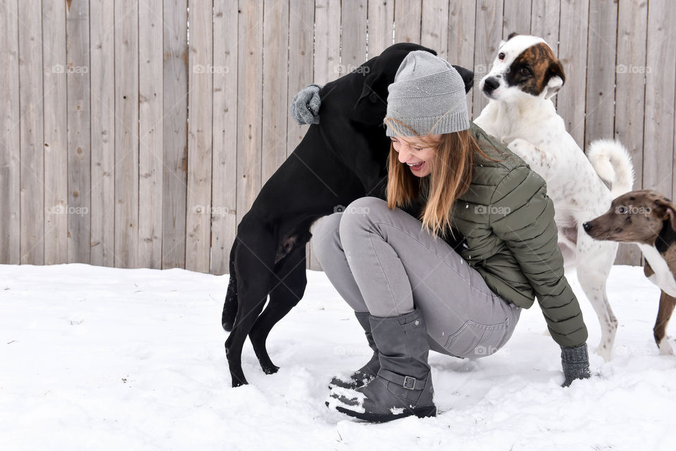 Young millennial woman playing with her dogs in the snow