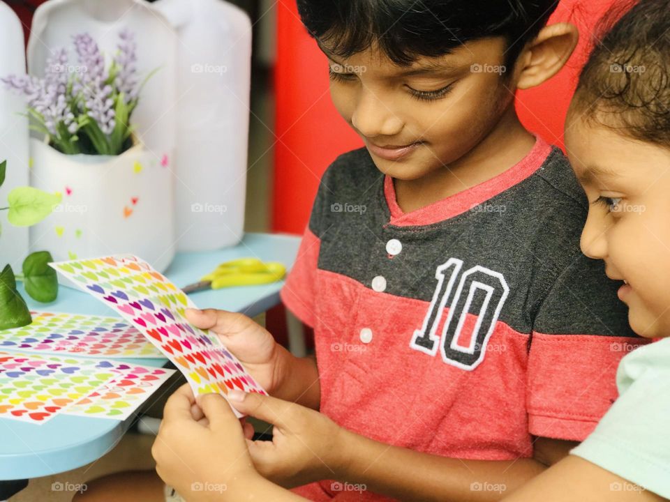 A boy and girl making leftover milk bottle craft and they paste some stickers on it.