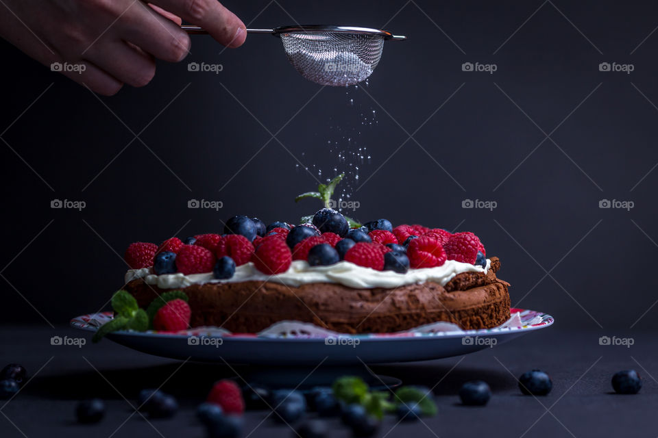 Person's hand holding strainer over the cake