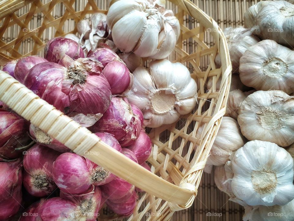 A bundle of organic Thai garlic and shallots the most widely used ingredients in Thai cuisine in a handmade basket on a bamboo mat - Top view closeup