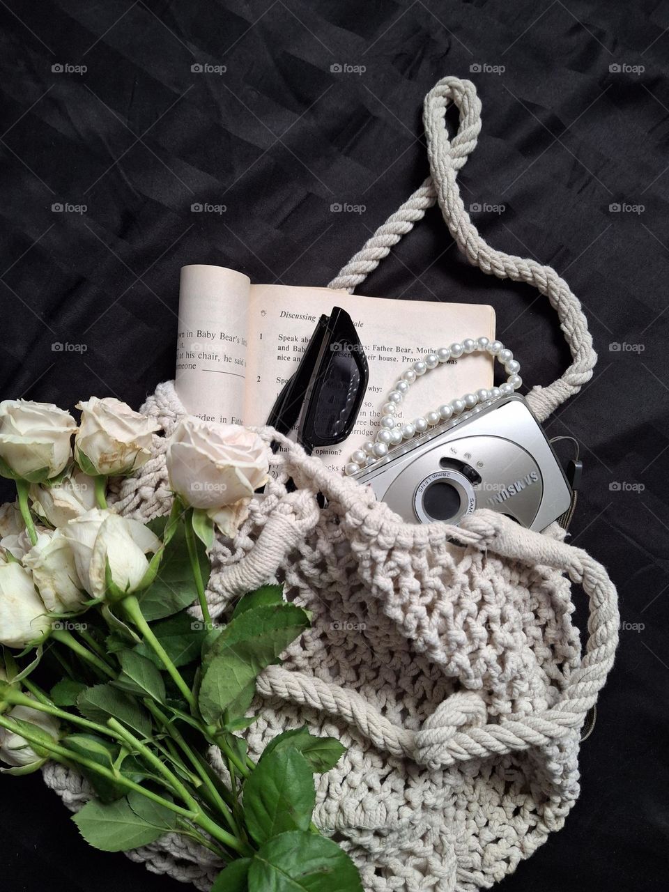 knitted vintage bag with a bouquet of flowers, namely white roses, and retro accessories on a black background