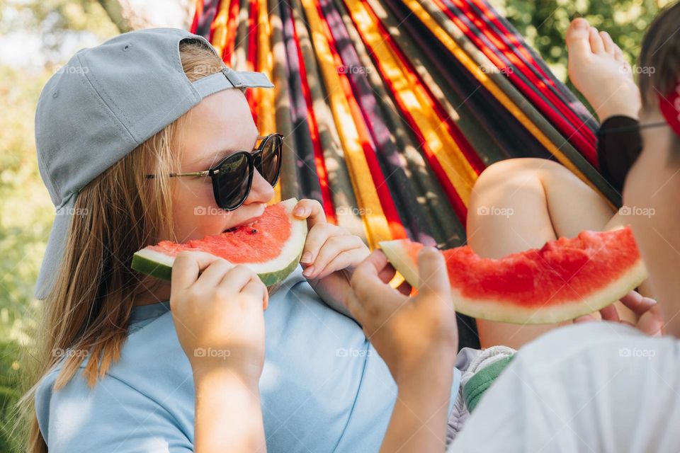 Kid teen girl eating watermelon in hammock. Summer food 