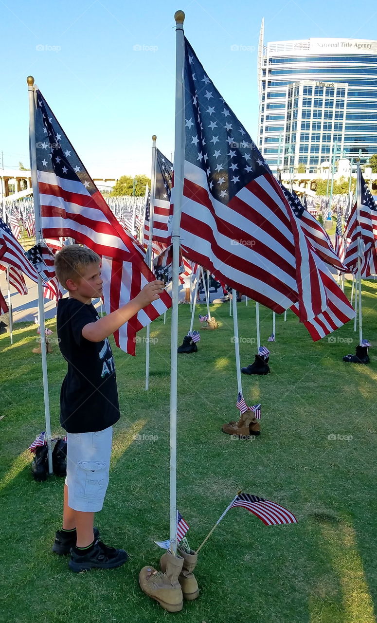 Young boy standing near American flag in field