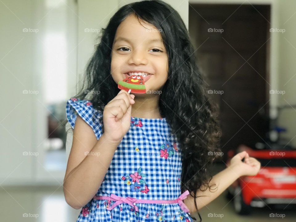 A four year old girl eating watermelon candy lollipop and smiling very beautifully.