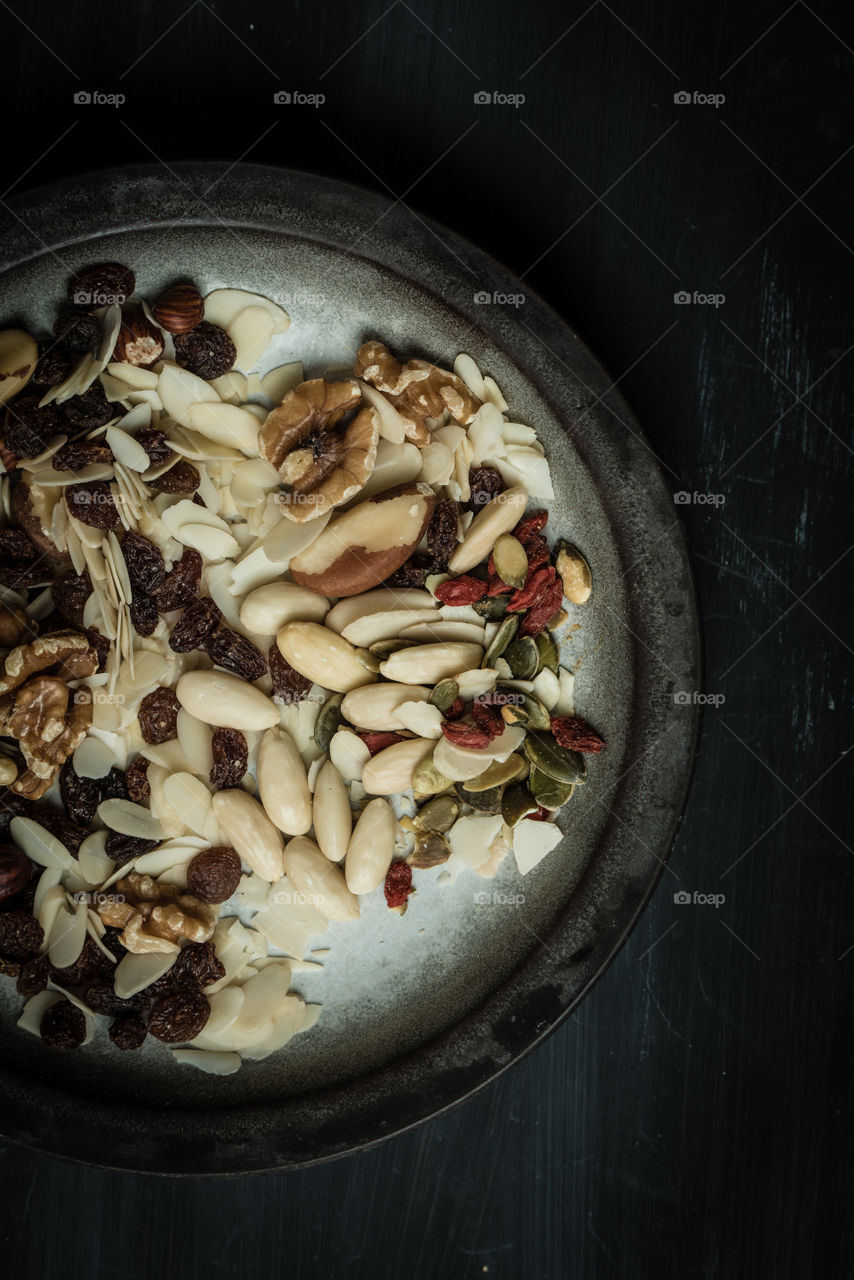 dark food photography. rustic, black, wooden table with vintage plate full of nuts. top view