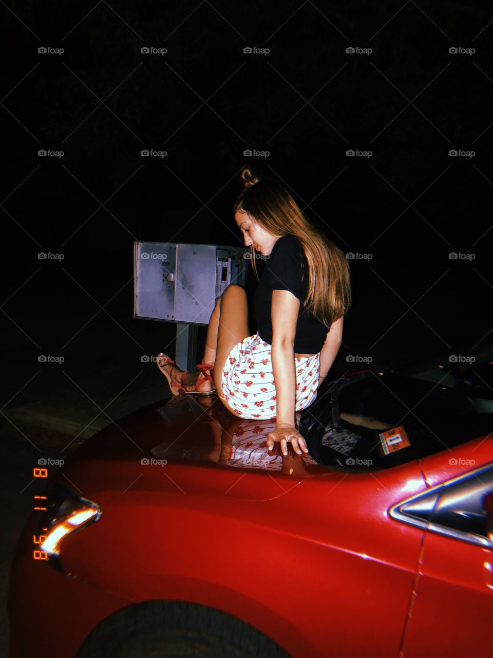 Female sitting on hood of red car at night