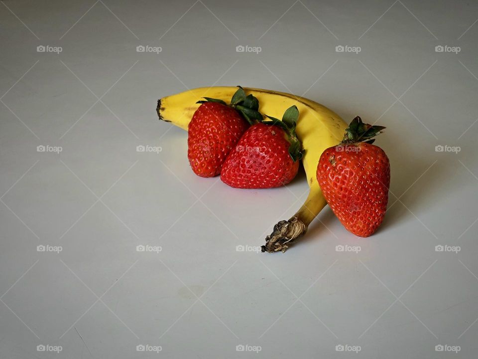 A banana and some strawberries placed on a table with a white background.