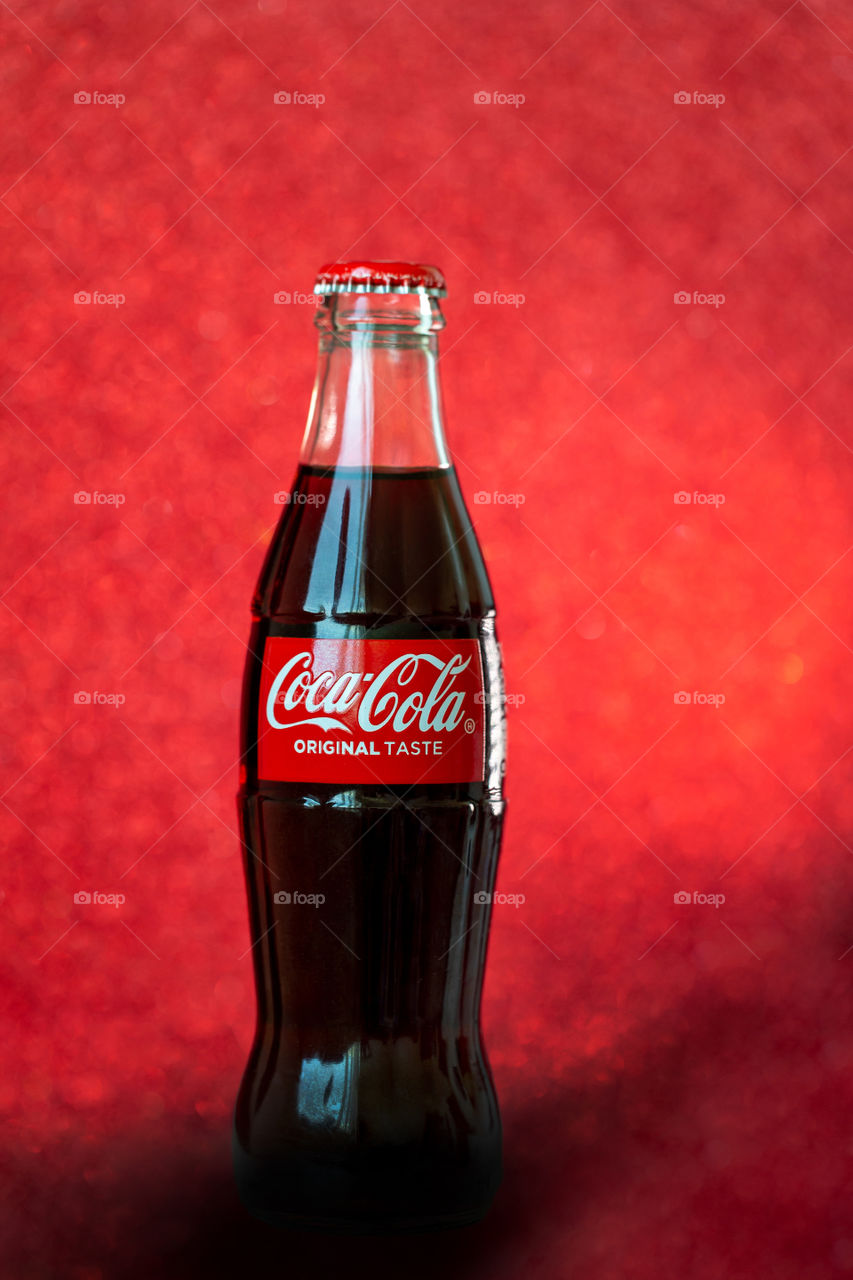 Coca-cola glass bottle on red glitter background, vertical shot