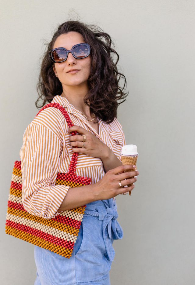 Young millennial woman, wearing a colorful outfit, while eating an icecream during summer season.