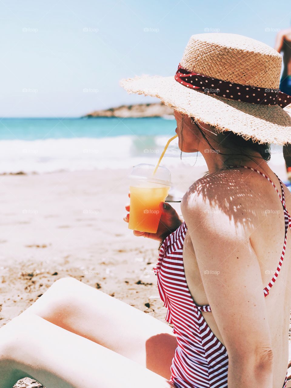 Girl in the straw hat drinking juice on the beach