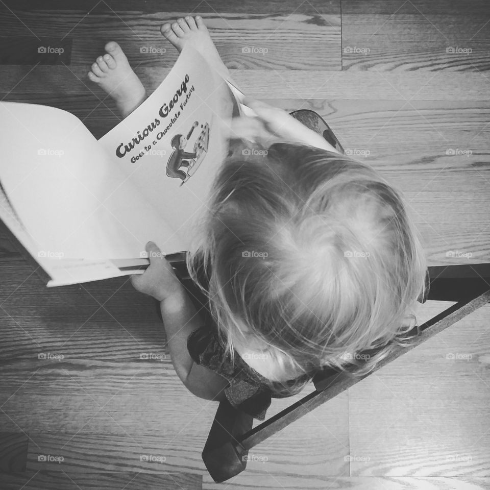 A black and white photo of of young child reading the story of Curious George.
