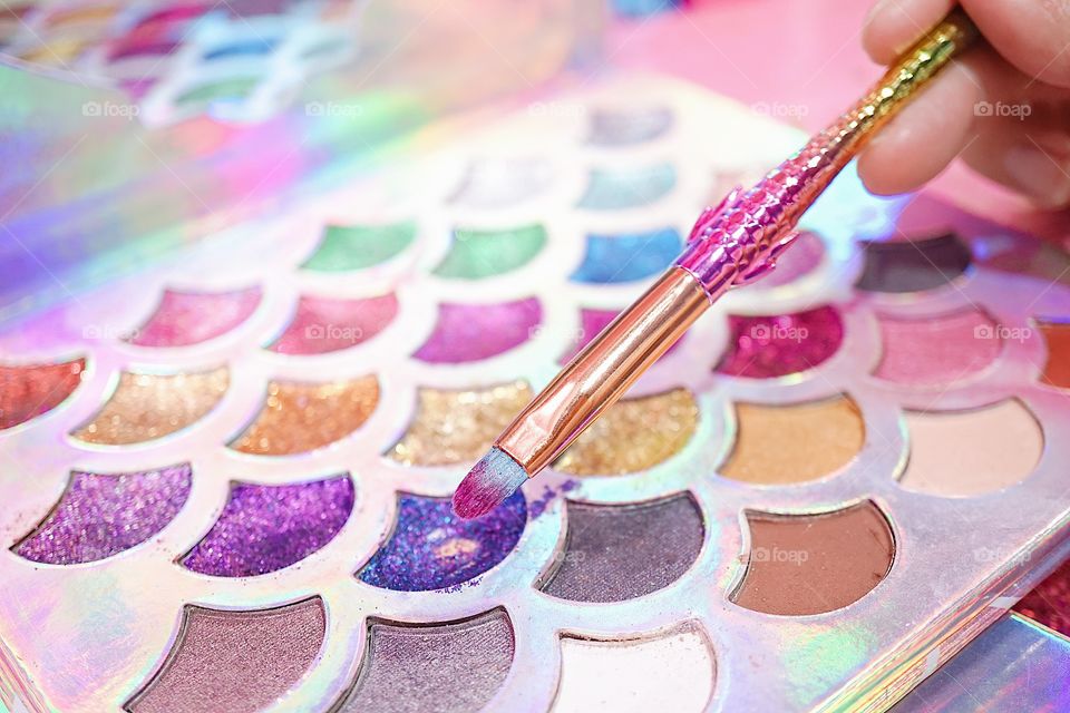 Eye shadow palette. Cosmetic for lady. Colorful and glitter eye shadow palette in mermaid fairy tales concept. With soft focus on the brush. 