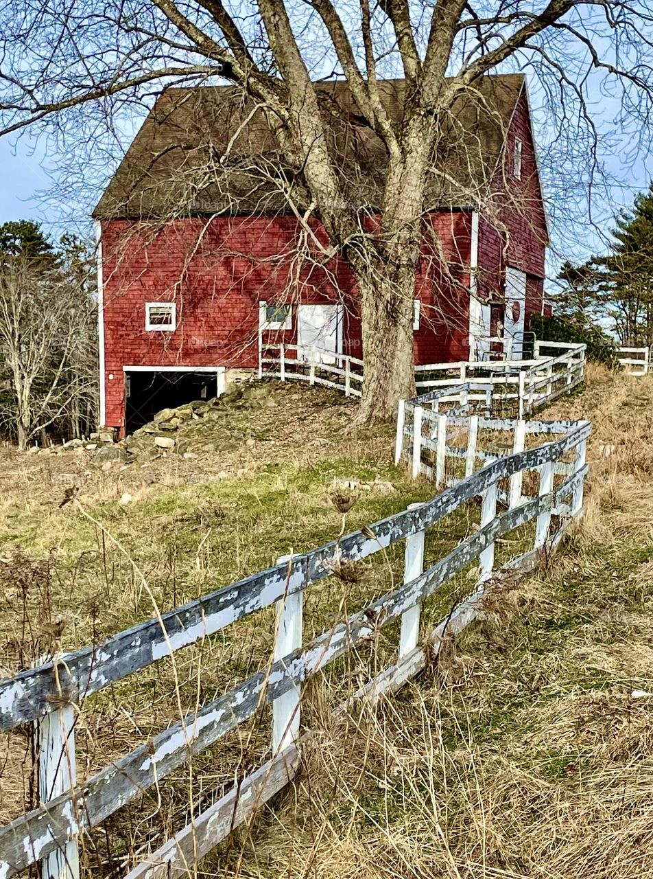 An old fence meanders up a hill toward a red barn.