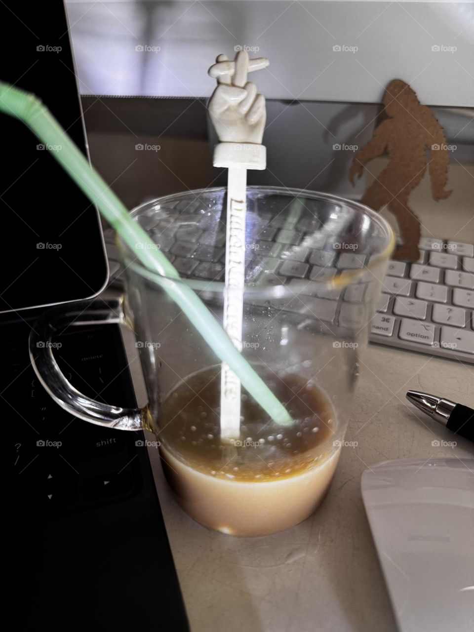 Glass cup with iced Starbucks, green plastic straw and vintage white plastic swizzle stick with hand holding cigarette, on desktop with computer, iPad, keyboard, mouse and pen