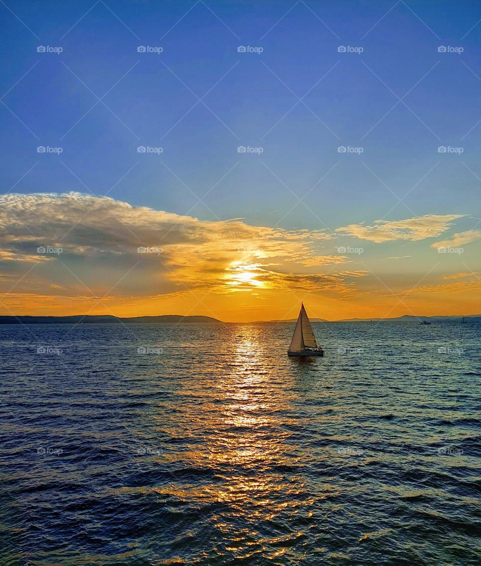 A wonderful sunset on the open sea on which a lonely sailboat sails. Summer sea landscape