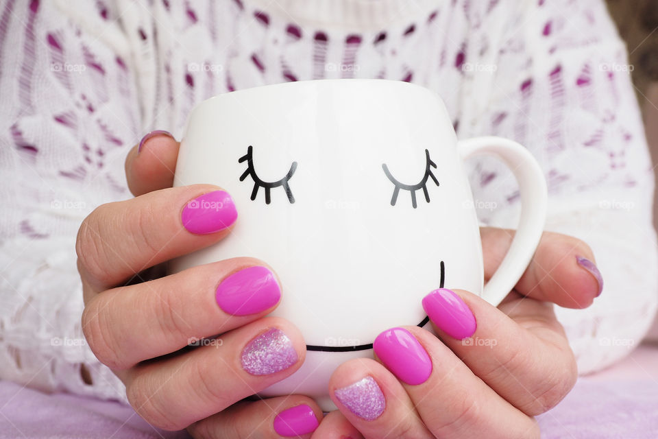 women's hands with a bright manicure hold a mug with a given face