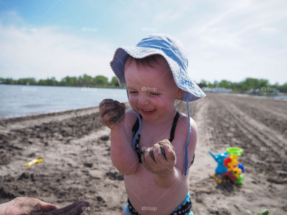 Toddler girl at the beach is delighted by the sand she is squishing in her hands.
