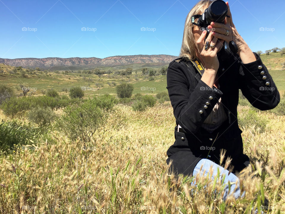 Female FOAP photographer (me) in the Australian outback in the Flinders Ranges of south Australia, camera in hand, capturing a photo while the light was just right. In this case a group of wild emu. Behind me, a part of the mountain ranges known as Wilpena Pound, 