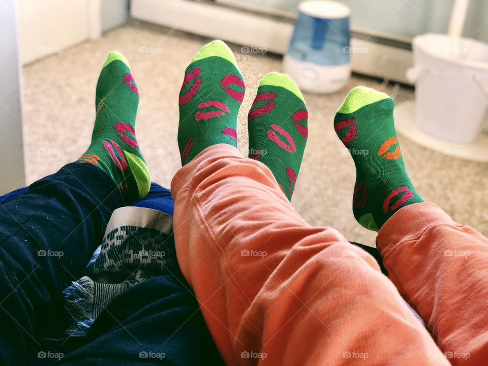 Couple celebrating Valentine’s Day with lip socks, couple laying on bed together, couple wearing matching socks, couple in love, comfy clothes on couple 