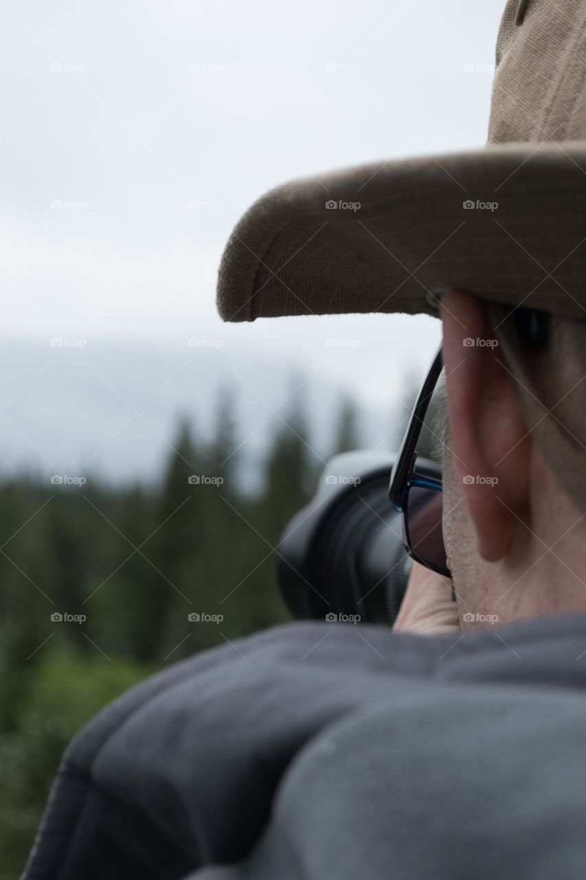 Back view head shot male photographer in hat shooting outdoors with DSLR camera 