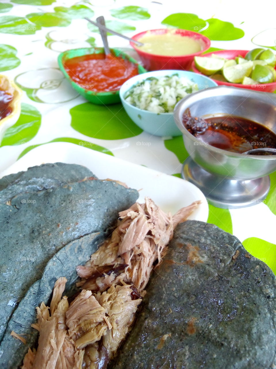 tacos de barbacoa de borrego con tortilla azul hecha a mano, de fondo salsas, limones y condimentos