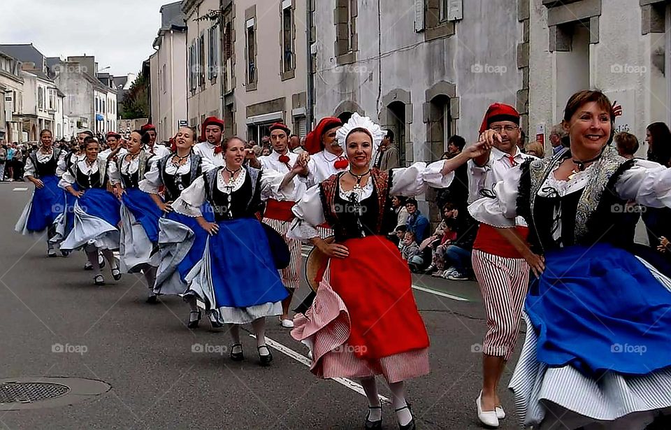 A dancer's parade of men and women dressed in Breton traditional costumes dancing at the Filets Bleus Festival in a street of Concarneau