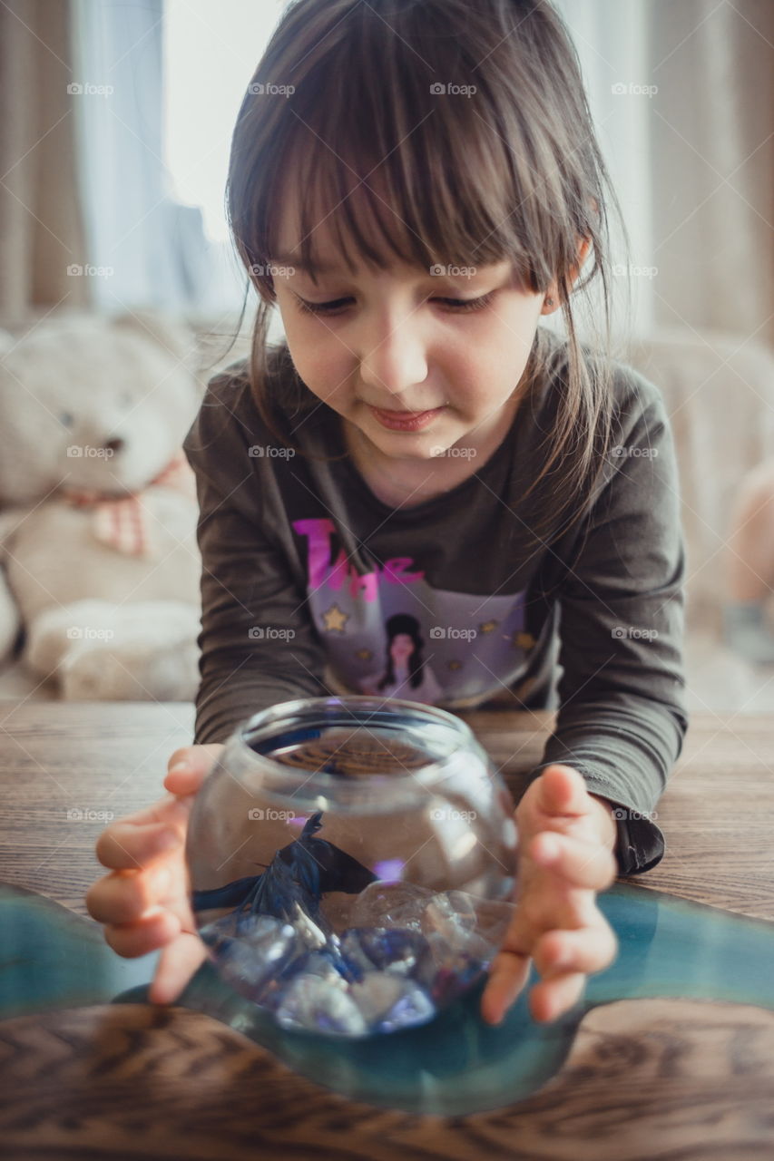 Little girl with fish in round aquarium at home