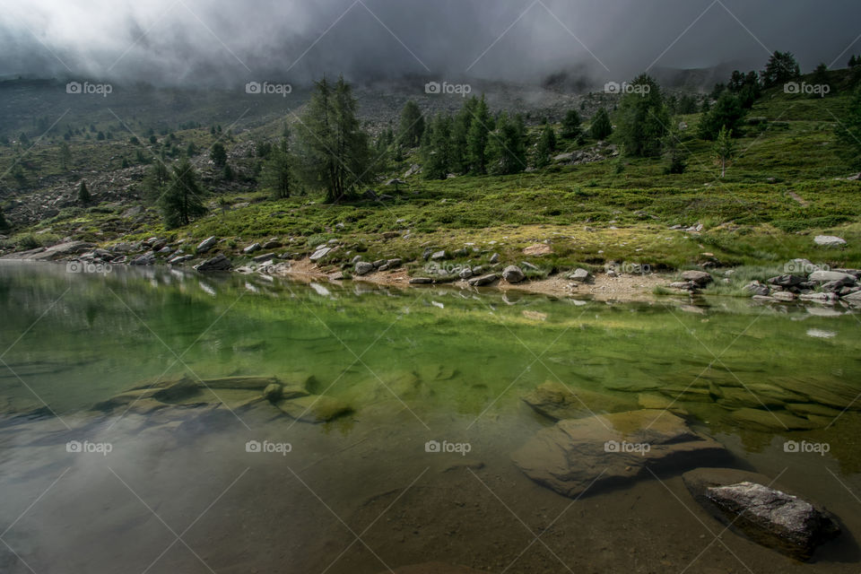 An alpine pond shows it's green reflections amidst a cloudy day