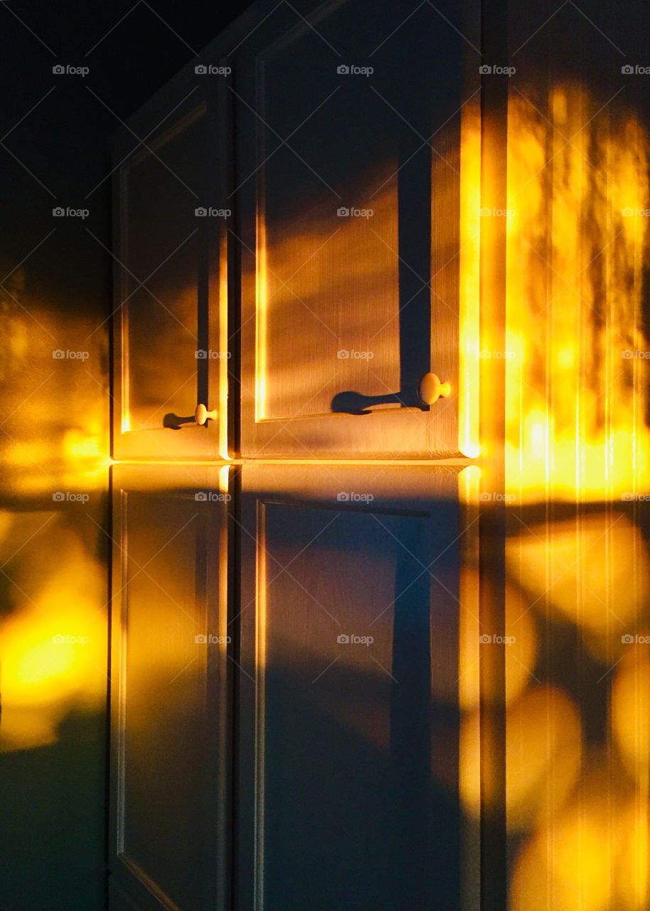 Golden sunlight streaming onto white cabinets in the interior of a home, shadows from tree branches outside 