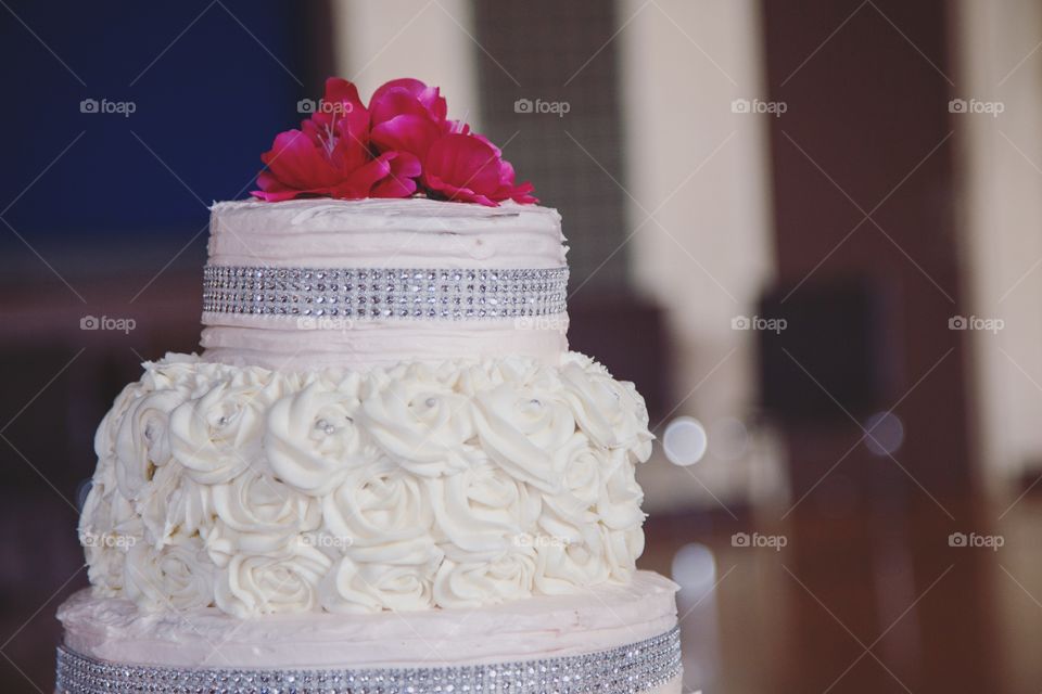 A fancy cake with massive pink flowers and decorated with glitter and white flowers