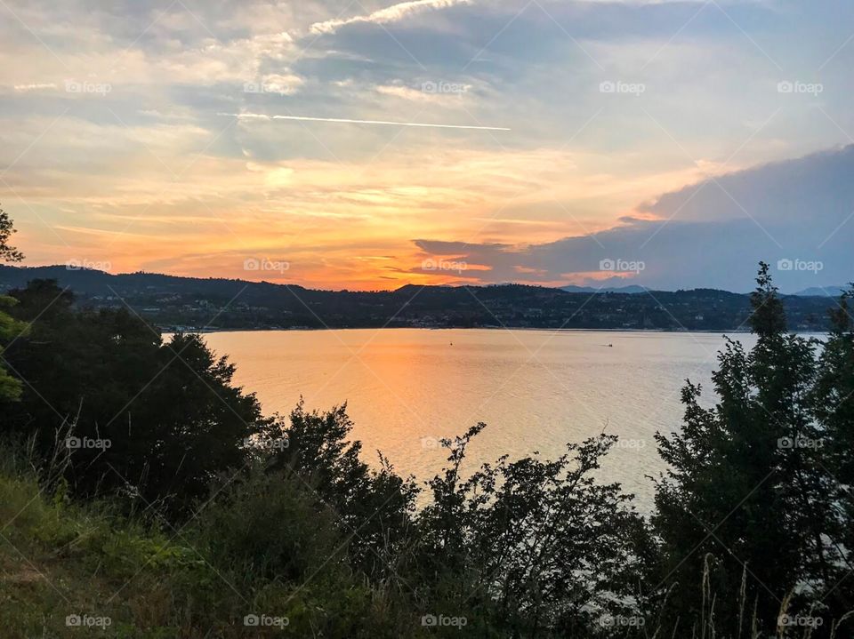 The sunlight shines an orange in the sky and reflects the color into the water lake, lakeside has mountains and trees. I am sitting and watching this wonderful landscape.