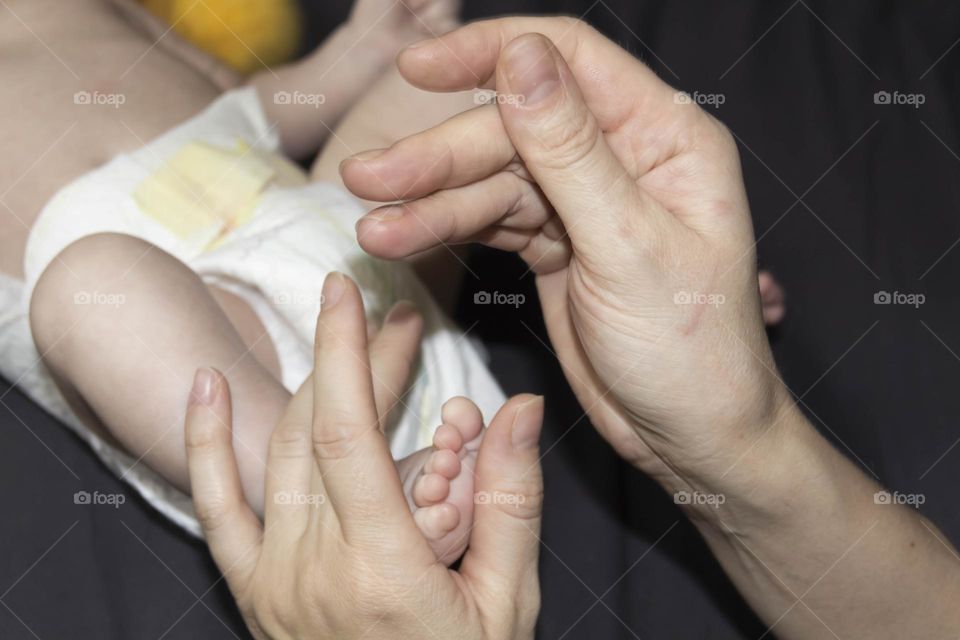 A happy mother in white holds the legs of a newborn baby in her hands. Lifestyle and newborn.