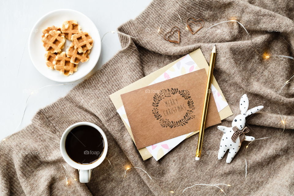 Flatlay items: cup of coffee, plate with cookies, card merry Christmas, pencil, rabbit toy 