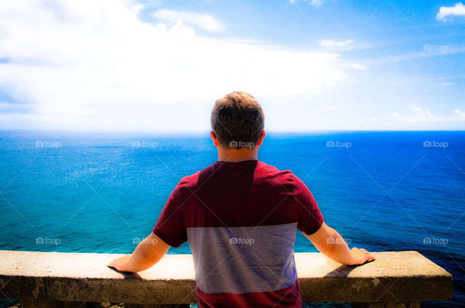 A young man looking out across a vast blue ocean.