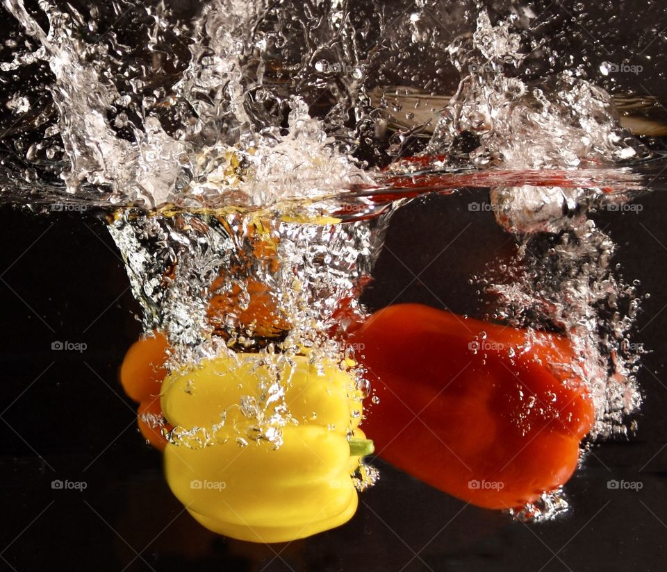 Colorful bell peppers splashing into water with a black background 