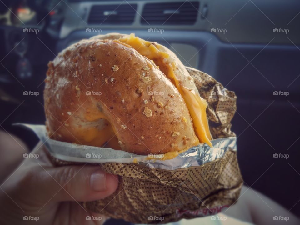 Chicken and cheese on a whole wheat bagel held in a hand wrapped in paper in a car fast food sandwich