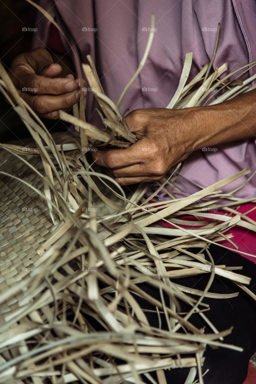A hand of a senior woman in her house in the village weaving the pandan leaves to make a mat