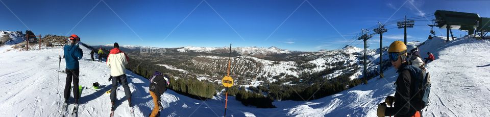 Panoramic photo at the top of a ski lift sounded by beautiful snowy mountains and trees