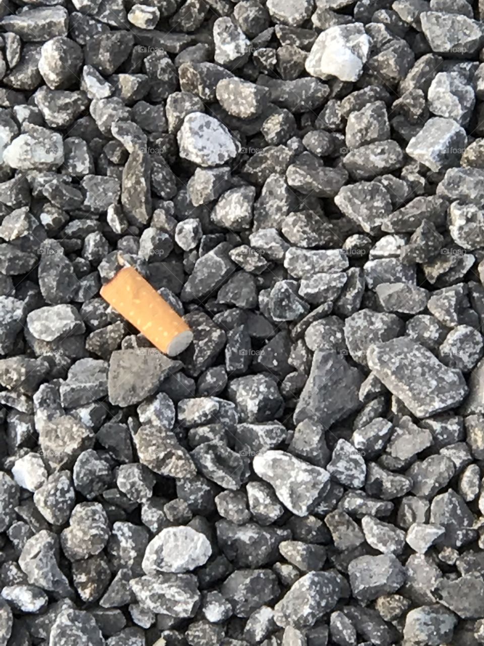 Cigarette butt thrown down on rock gravel in park