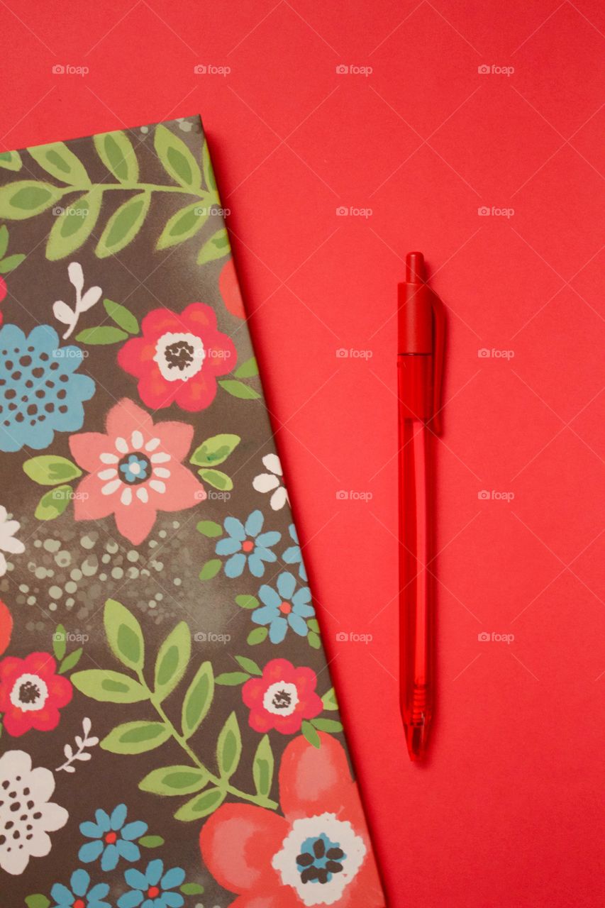 Flat lay of a multi-colored floral binder and red pen on a red background 