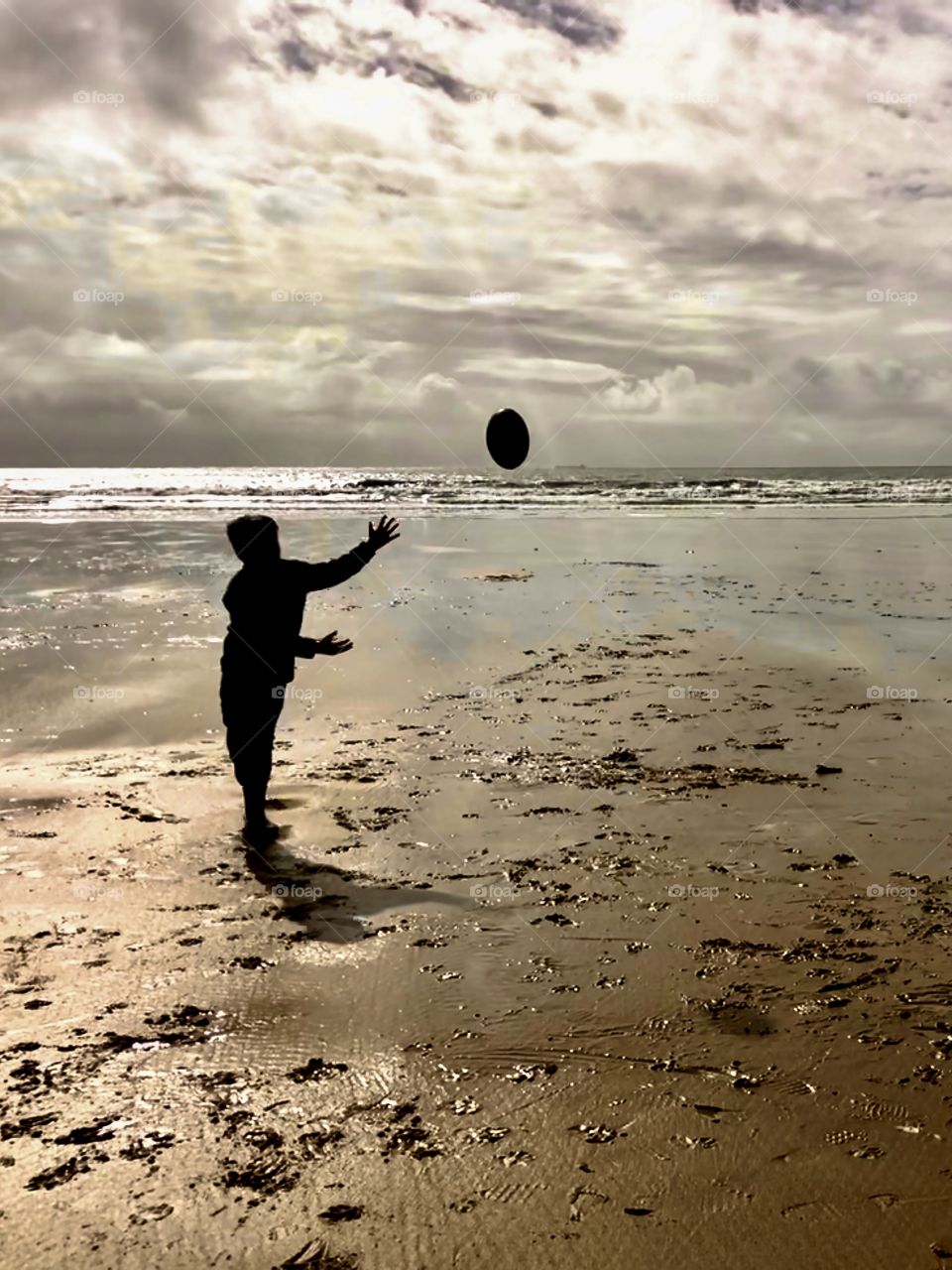 Silhouette of boy playing rugby on beach