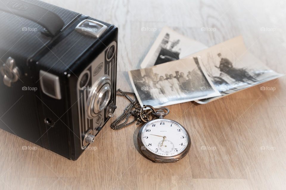 Old camera and pocket clock with some black and white photos on wooden table in vintage mood 