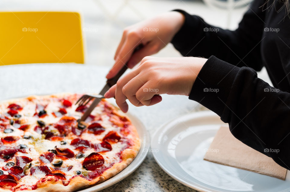 Girl's hands cutting a pepperoni pizza in a cafe.